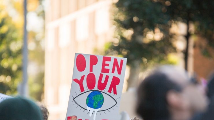 Climate Change protester holds sign saying Open your Eyes at student global warming environmental protest in Melbourne