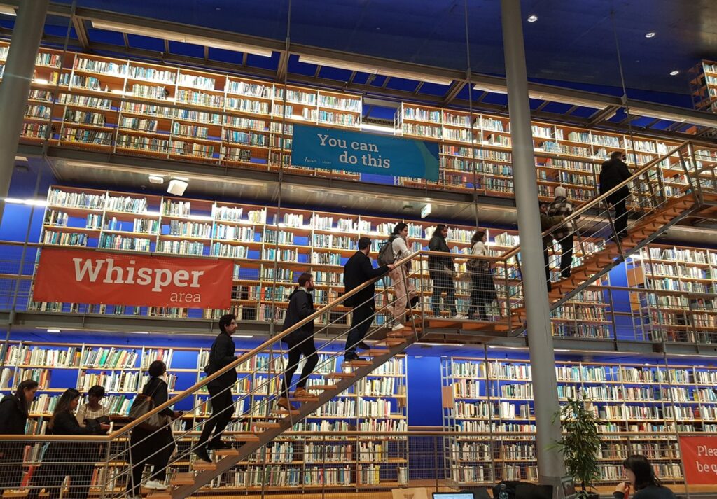 How can I apply for MBA programs? Line of students in library make their path.